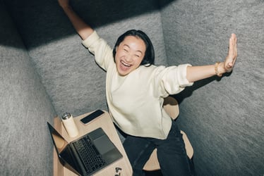 Femme souriante, les bras écartés, dans un espace de travail insonorisé.
